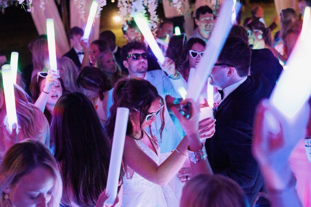 Bride and groom laughing together in heart-shaped sunglasses surrounded by glow sticks