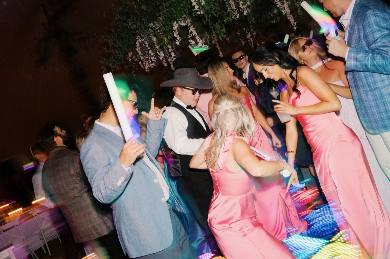 Wedding guests dancing under string lights and greenery