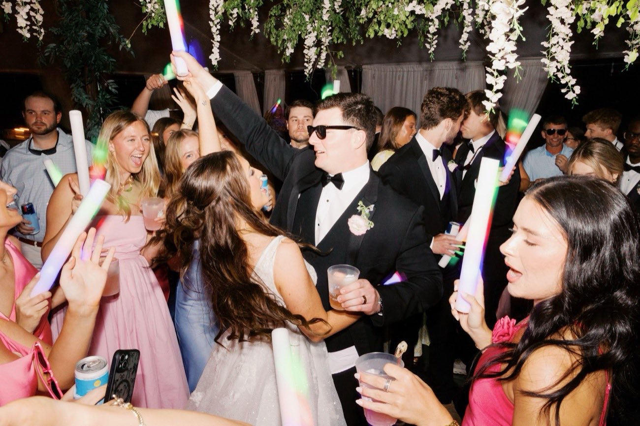 Bride and groom surrounded by cheering guests with glow sticks raised