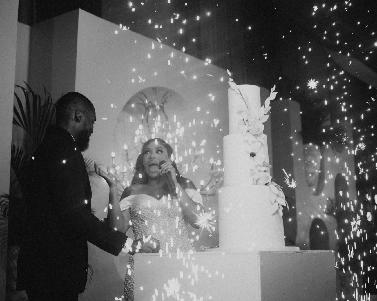 Bride reacting with joy as cold spark fountains erupt beside the wedding cake